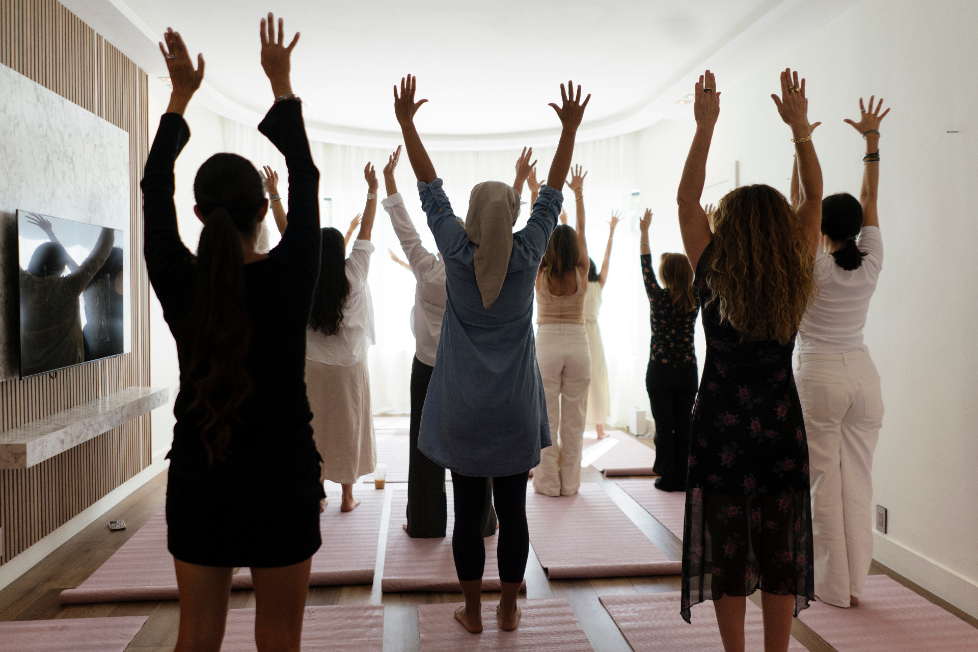 Women of One Container standing in a sunlit room, arms raised overhead in a gesture of opening and expansion.